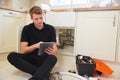 Young plumber with tablet computer fixing sink in kitchen