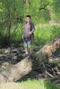 A young plump man stands on the trunk of an rickety tree. Near windbreak. In the park among the bright green foliage