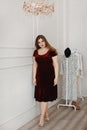 Young plus size model girl in red velvet dress posing in the studio. Young plump woman with nude makeup in modish dress