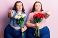 Young plus size twins holding flowers pointing with finger to the camera and to you, confident gesture looking serious Royalty Free Stock Photo
