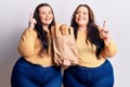 Young plus size twins holding paper bag with bread surprised with an idea or question pointing finger with happy face, number one Royalty Free Stock Photo