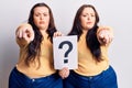 Young plus size twins holding question mark pointing with finger to the camera and to you, confident gesture looking serious Royalty Free Stock Photo