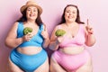 Young plus size twins wearing bikini holding broccoli smiling with an idea or question pointing finger with happy face, number one Royalty Free Stock Photo