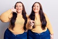 Young plus size twins wearing casual clothes smiling doing talking on the telephone gesture and pointing to you Royalty Free Stock Photo