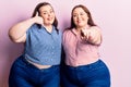 Young plus size twins wearing casual clothes smiling doing talking on the telephone gesture and pointing to you Royalty Free Stock Photo