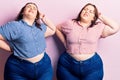 Young plus size twins wearing casual clothes suffering of neck ache injury, touching neck with hand, muscular pain Royalty Free Stock Photo