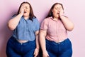 Young plus size twins wearing casual clothes yawning tired covering half face, eye and mouth with hand