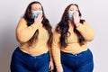 Young plus size twins wearing medical mask bored yawning tired covering mouth with hand