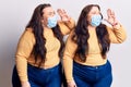 Young plus size twins wearing medical mask shouting and screaming loud to side with hand on mouth