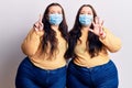 Young plus size twins wearing medical mask showing and pointing up with fingers number six while smiling confident and happy Royalty Free Stock Photo