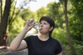 Young plus size woman drinks water after jogging in the summer park. Drinking regime during sports Royalty Free Stock Photo