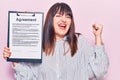 Young plus size woman holding clipboard with agreement document screaming proud, celebrating victory and success very excited with Royalty Free Stock Photo