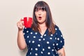 Young plus size woman holding coffee scared and amazed with open mouth for surprise, disbelief face Royalty Free Stock Photo