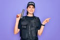 Young police woman wearing security bulletproof vest uniform and holding gun very happy pointing with hand and finger to the side Royalty Free Stock Photo