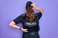 Young police woman wearing security bulletproof vest uniform over purple background Backwards thinking about doubt with hand on