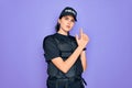 Young police woman wearing security bulletproof vest uniform over purple background Holding symbolic gun with hand gesture, Royalty Free Stock Photo