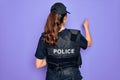 Young police woman wearing security bulletproof vest uniform over purple background Posing backwards pointing ahead with finger