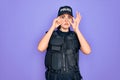 Young police woman wearing security bulletproof vest uniform over purple background Trying to open eyes with fingers, sleepy and Royalty Free Stock Photo