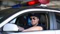 Young policeman in sunglasses sitting in car smiling into camera, important job