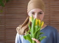 Young positive adult female cancer patient holding bouquet of yellow tulips, smiling and looking at camera.