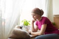 Young positive adult female cancer patient sitting in the kitchen by a window with her pet cat.