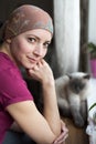 Young positive adult female cancer patient sitting in the kitchen by a window with her pet cat, smiling.