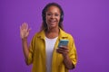 Young positive African American woman in headphones uses phone and waves hand Royalty Free Stock Photo