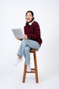 Young positive Asian woman sits on a chair with her laptop, on an isolated studio white background Royalty Free Stock Photo