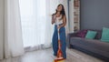 Young positive caucasian woman funnily dancing while cleaning the house