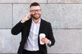 Young positive confident businessman speaking on mobile phone with take away coffee in hand Royalty Free Stock Photo