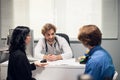 A young positive doctor receiving a teen patient with his parent at the office, he is asking questions and making notes