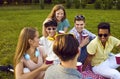 Young positive group of friends men and women vacationers and laughing on picnic in park