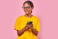 Young positive Indian woman in trendy glasses uses mobile phone stands in studio Royalty Free Stock Photo
