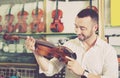 Young positive man purchasing traditional violins in store Royalty Free Stock Photo