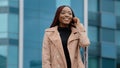 Young positive pretty african american woman standing against background of office building talking on phone answering Royalty Free Stock Photo