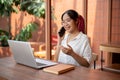 A positive Asian woman is talking on the phone with her client while working remotely at a cafe Royalty Free Stock Photo