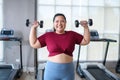 Young, Positive, Smiling, Cheerful overweight woman training with dumbbells in gym. Fat woman in sportswear doing fitness exercise Royalty Free Stock Photo