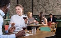 Young positive smiling woman with African American colleague on friendly meeting over dinner with wine in restaurant