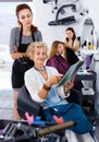 Young woman hairdresser in hair salon helping to senior woman ch