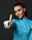 Young positive woman doctor in blue working uniform and latex gloves showing forefinger to camera Royalty Free Stock Photo