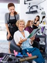 Young woman hairdresser in hair salon helping to senior woman ch