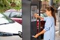 Young woman paying for parking in modern parking meter on city street Royalty Free Stock Photo