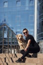 Young positive woman sitting on stairs with her dog when have a walk outdoors near business building Royalty Free Stock Photo