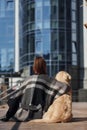 Young positive woman sitting on stairs with her dog when have a walk outdoors near business building Royalty Free Stock Photo