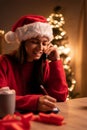 Young positive woman with smartphone doing online shopping during Christmas holidays, smiling female freelancer talking Royalty Free Stock Photo