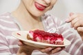 Young positive woman is tasting a piece of cheesecake with raspberries, sweet food Royalty Free Stock Photo