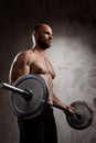 Young powerful sportsman training with barbell over dark background.