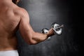 Young powerful sportsman training with dumbbells over black background.