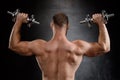 Young powerful sportsman training with dumbbells over black background.