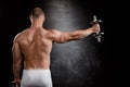 Young powerful sportsman training with dumbbells over black background.